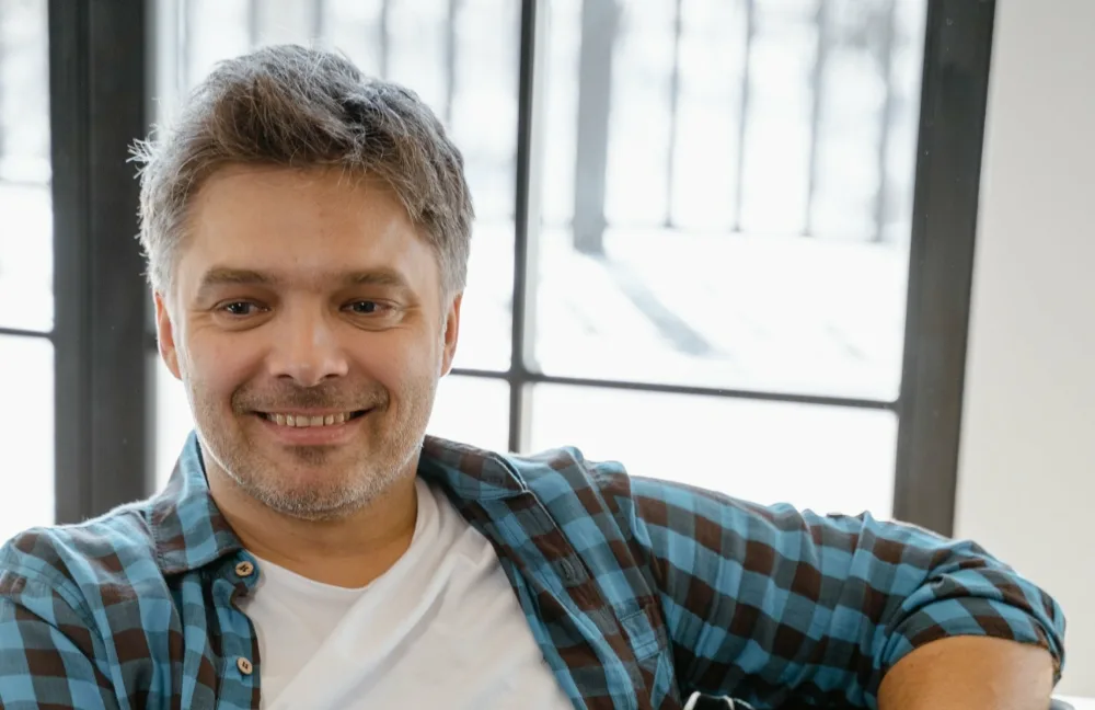 Hombre de unos 45 años sonriendo en el sofá de su casa con el portátil, informándose sobre vender la nuda propiedad con usufructo temporal